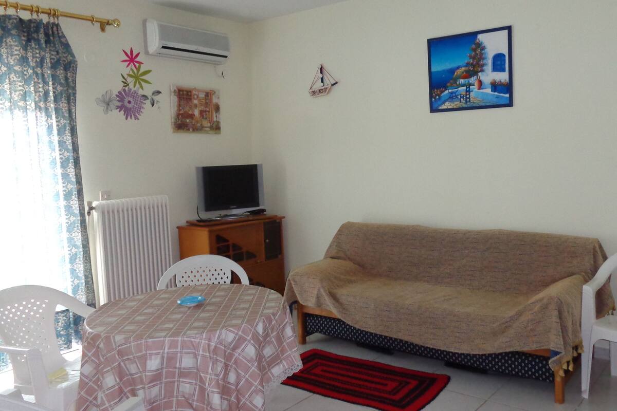 Un salón con sofá, televisor sobre un mueble, una mesa con mantel y alfombra roja.