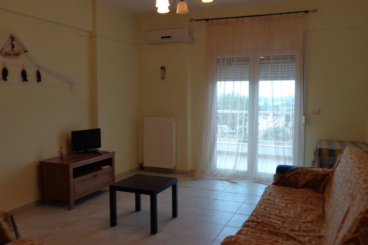 Una sala de estar con un sofá, un televisor sobre un mueble de madera, una mesita, un radiador y una ventana con cortinas.