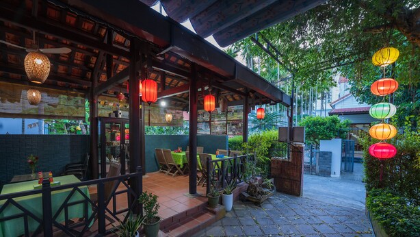 An outdoor patio area with tables and chairs, potted plants, and hanging lanterns. - Countryside Moon Homestay (Da Nang)