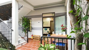 A hotel room with a bed, a small table with a vase of flowers, a chair, and a staircase leading to another room. - Countryside Moon Homestay (Da Nang)