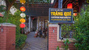 A sign for a countryside moon homestay with a brick entrance, a tiled pathway, and a bicycle parked outside. - Countryside Moon Homestay (Da Nang)