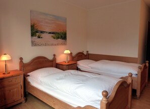 Una habitación con dos camas de madera, cada una con una mesita de noche y una lámpara. Hay un cuadro en la pared sobre las camas.