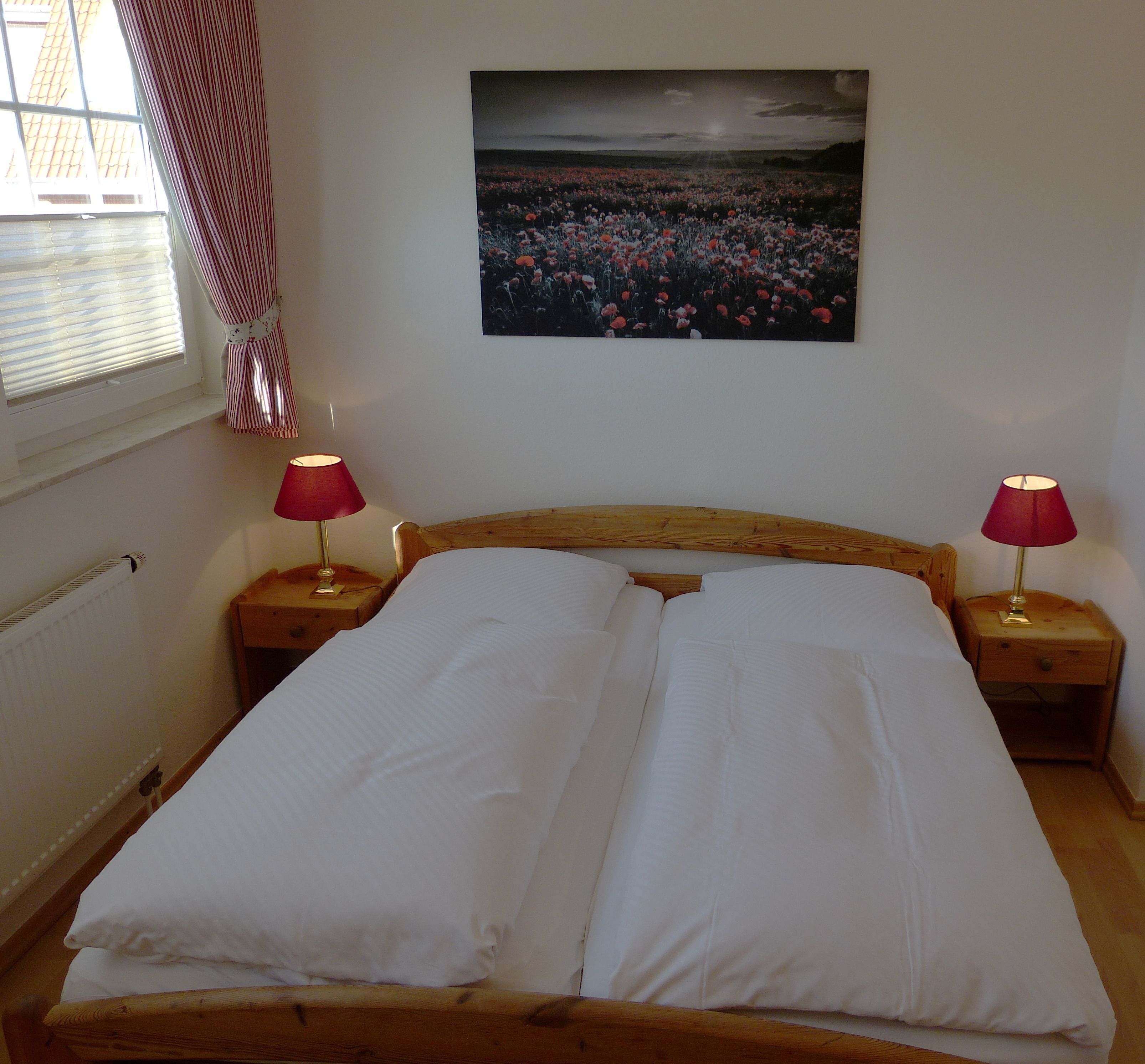 A bedroom with a wooden bed, two bedside tables with lamps, a window with blinds, and a painting on the wall.