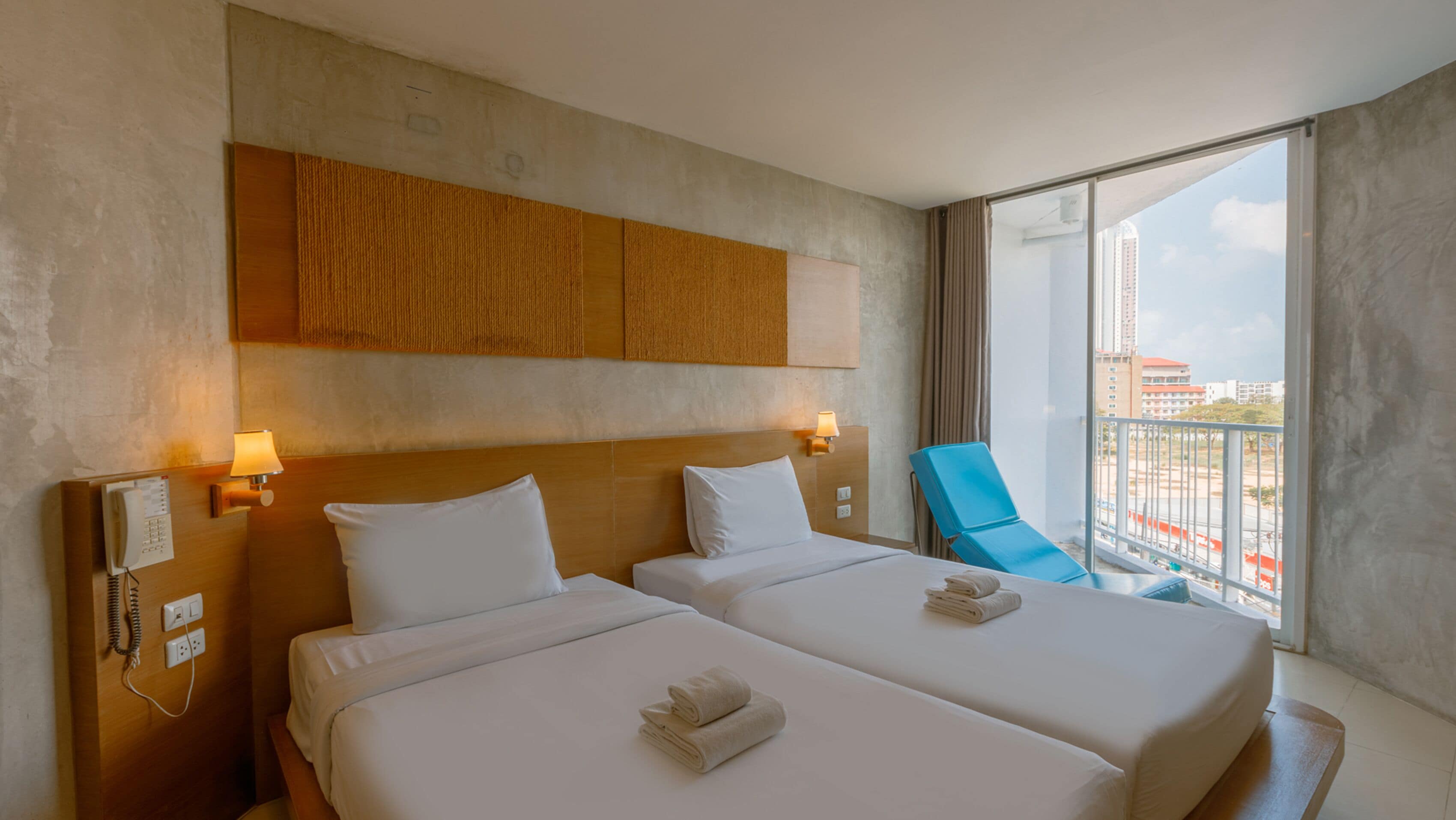 A hotel room with two beds, a wooden headboard, bedside lamps, a phone, and a view of the city through a large window.