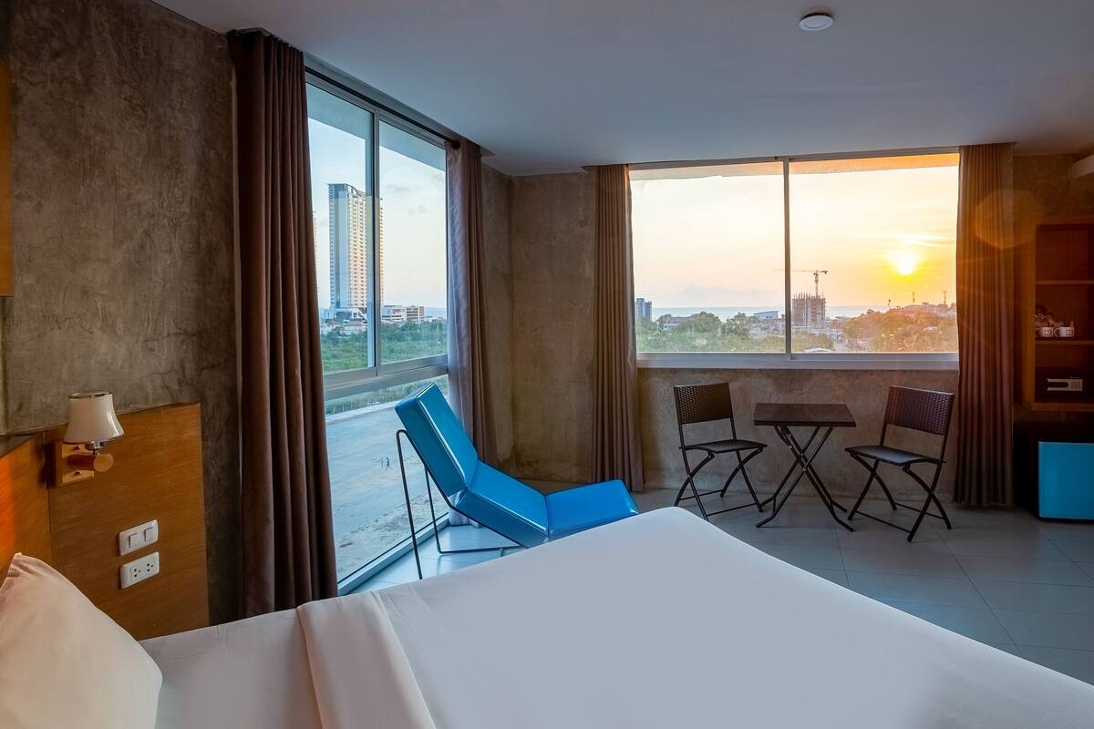 A hotel room with a large bed, a balcony with a view of the city, a small table with two chairs, and a wardrobe.