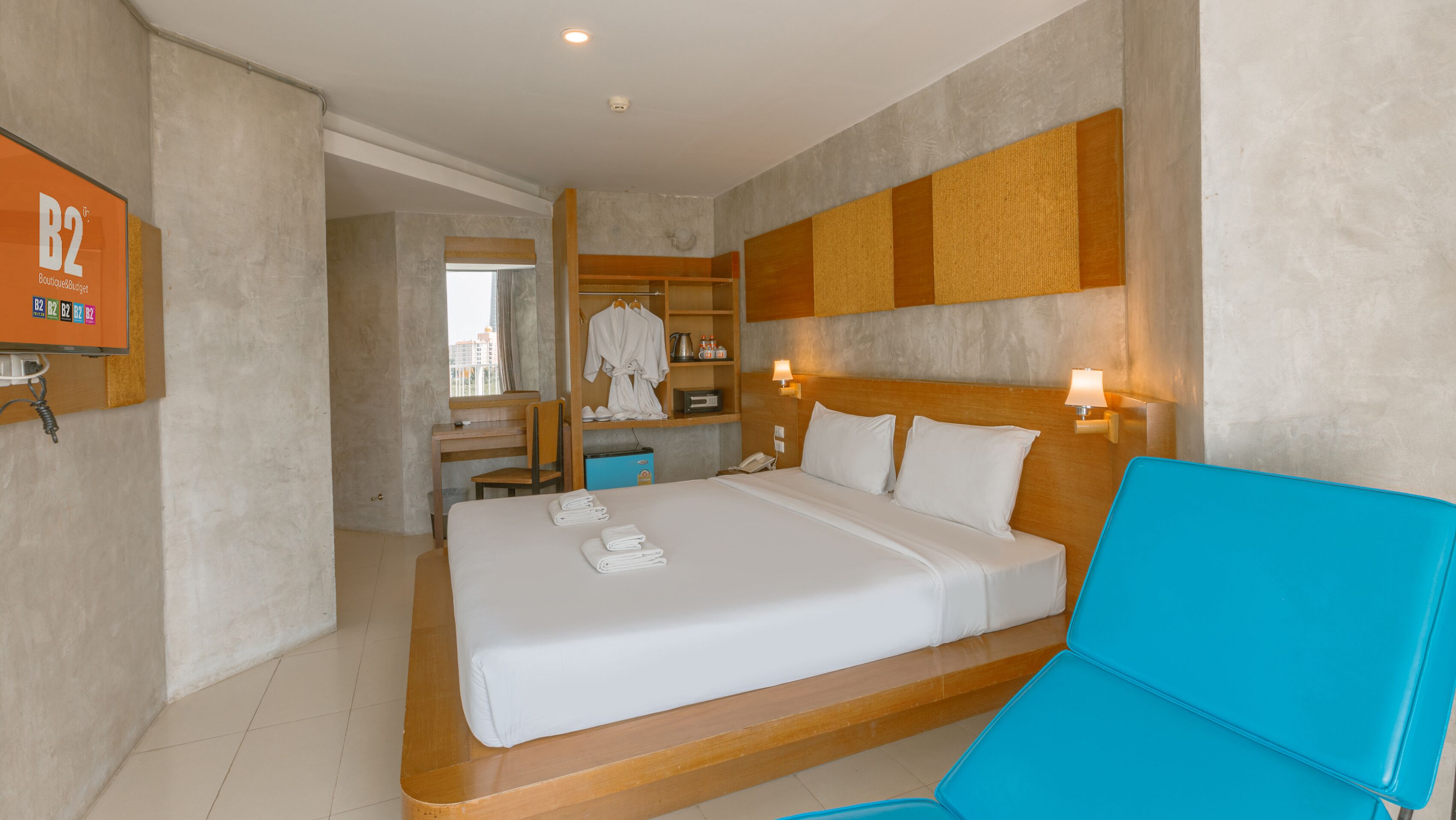 A hotel room with a large bed, a desk, a chair, a robe, and a TV.