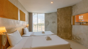 Quarto de hotel com duas camas, uma janela grande com vista para a cidade, uma televisão presa na parede e um telefone do lado esquerdo.