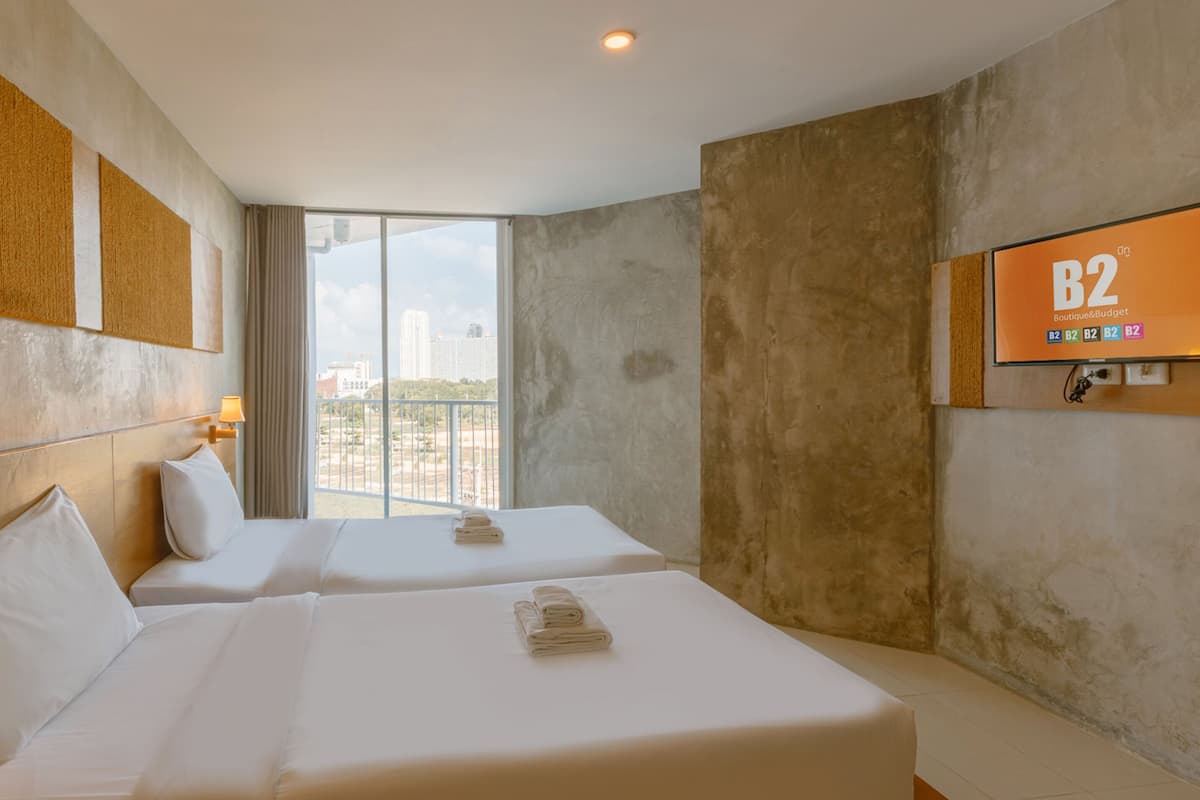 A hotel room with two beds, a large window with a city view, a mounted TV screen, and a telephone on the left side.