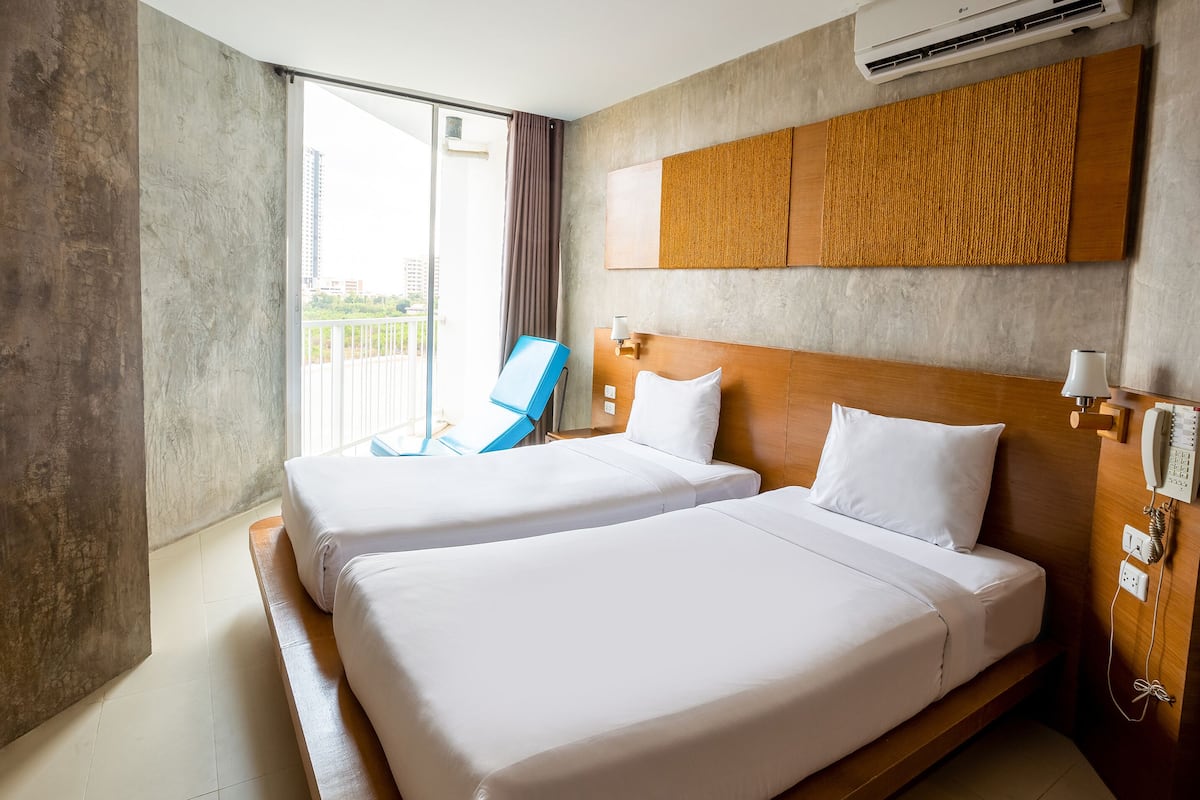 A hotel room with two beds, a large window, a blue chair, and a wooden headboard.