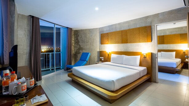 Quarto de hotel moderno com uma cama grande, uma varanda com vista para as luzes da cidade, uma cadeira azul e uma escrivaninha com artigos de higiene pessoal.