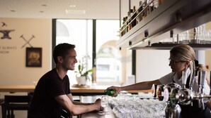A bar area with a bartender serving a customer. There are multiple glasses and bottles on the counter.