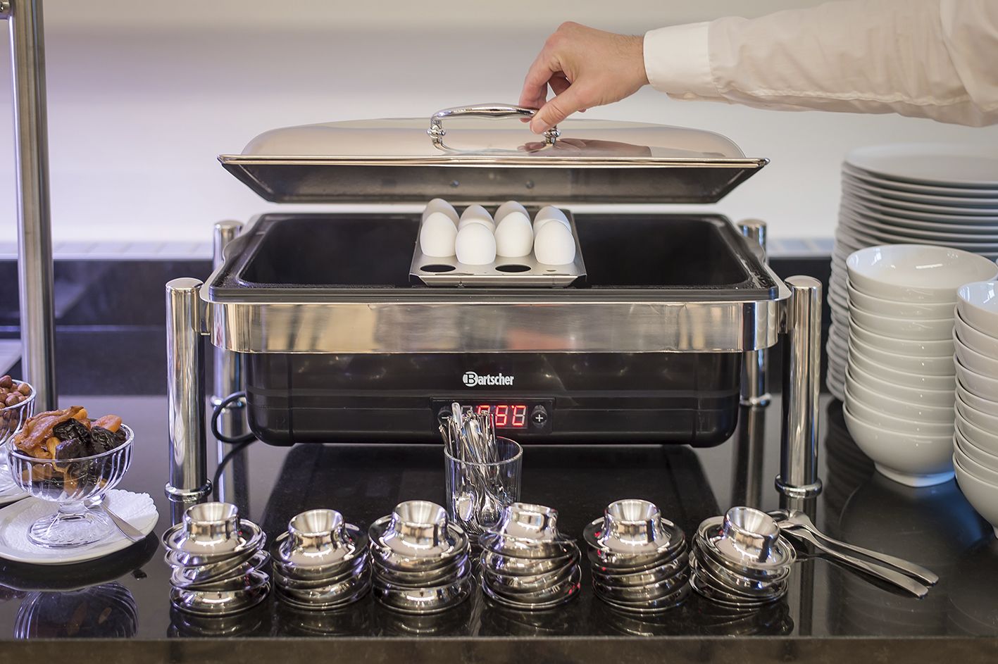 A coffee machine with a digital display, a stack of plates, and condiments.