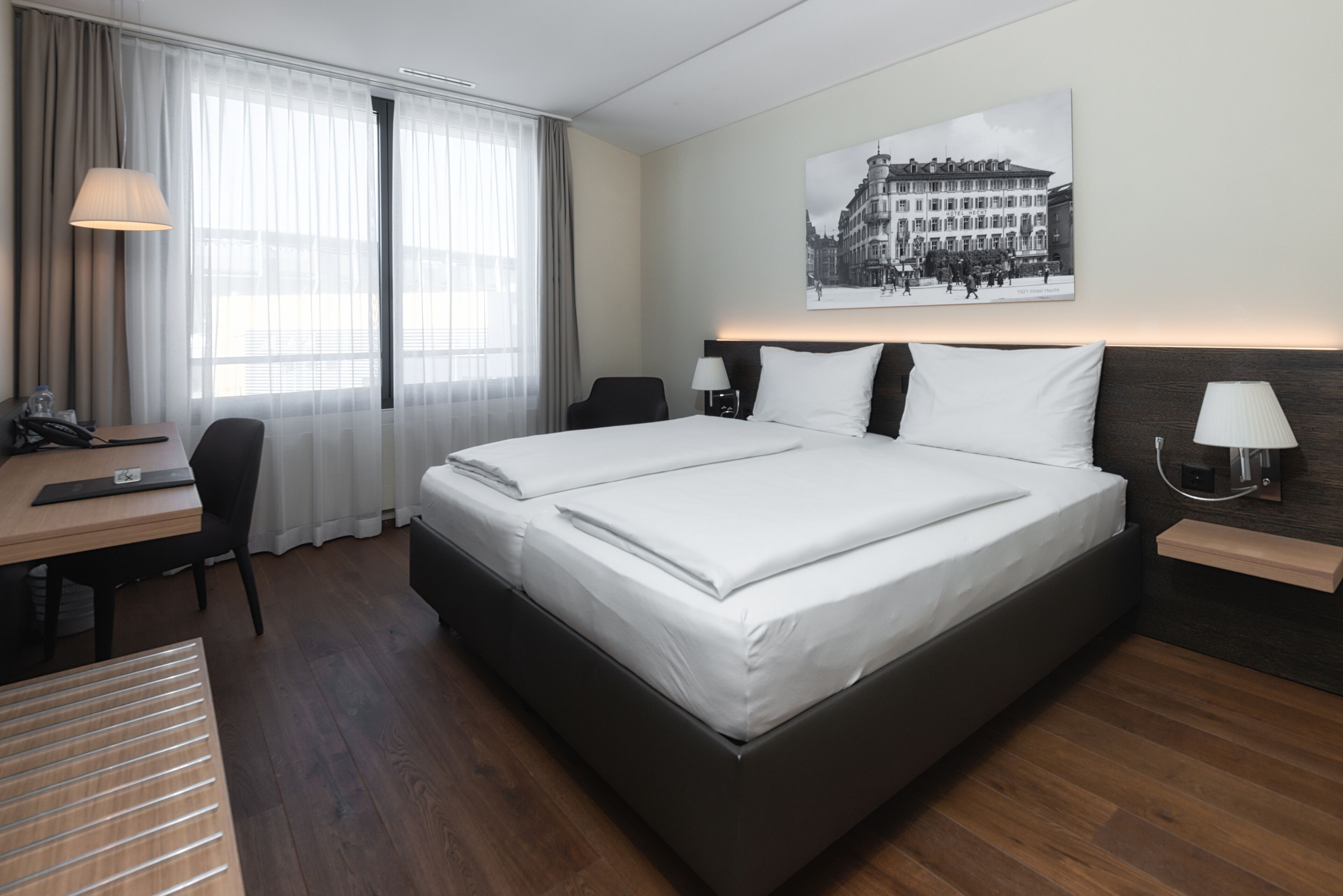 A hotel room with a large bed, a desk with a chair, a lamp, and a picture on the wall.