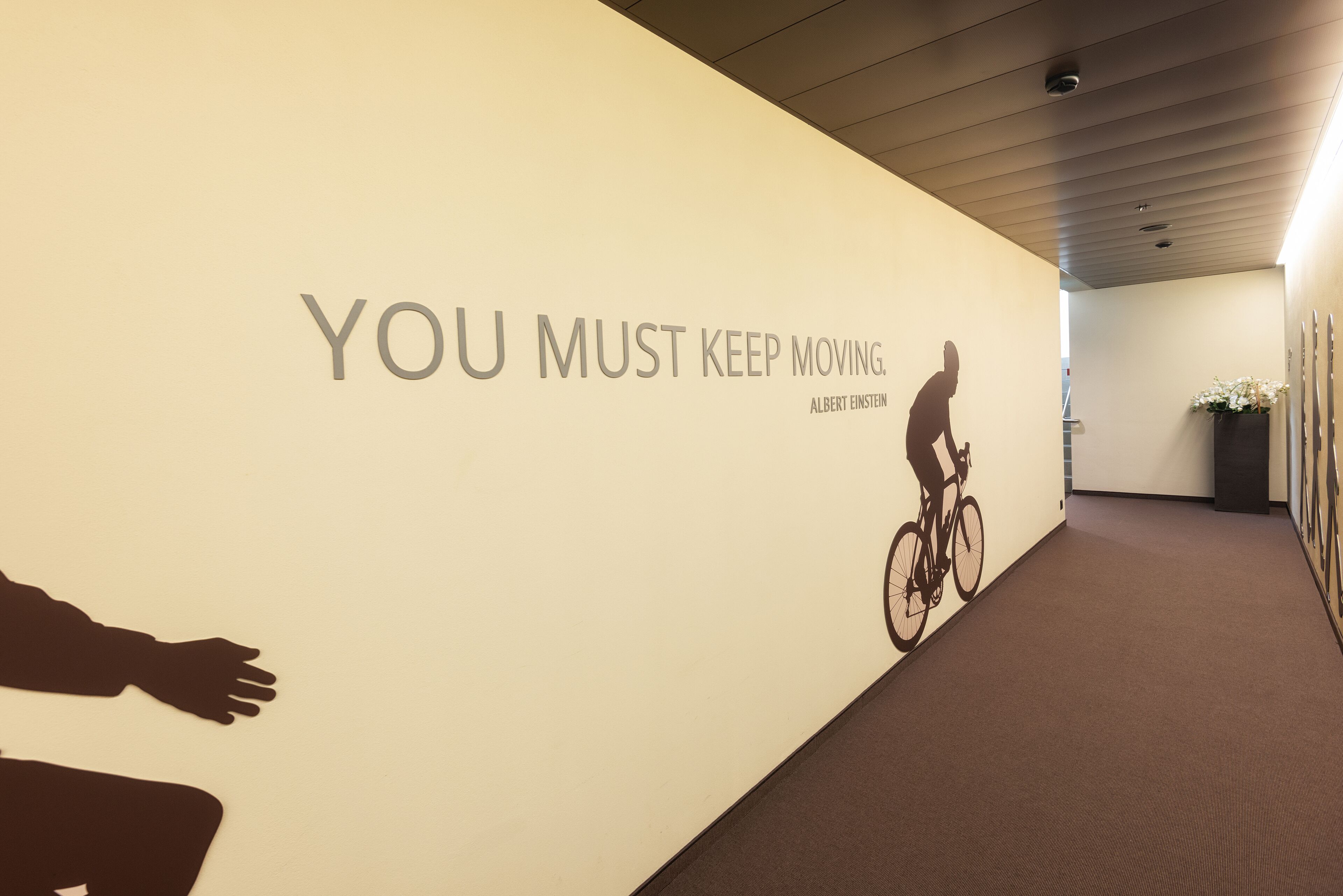 A hallway with a motivational quote on the wall, a cyclist silhouette, and a potted plant.