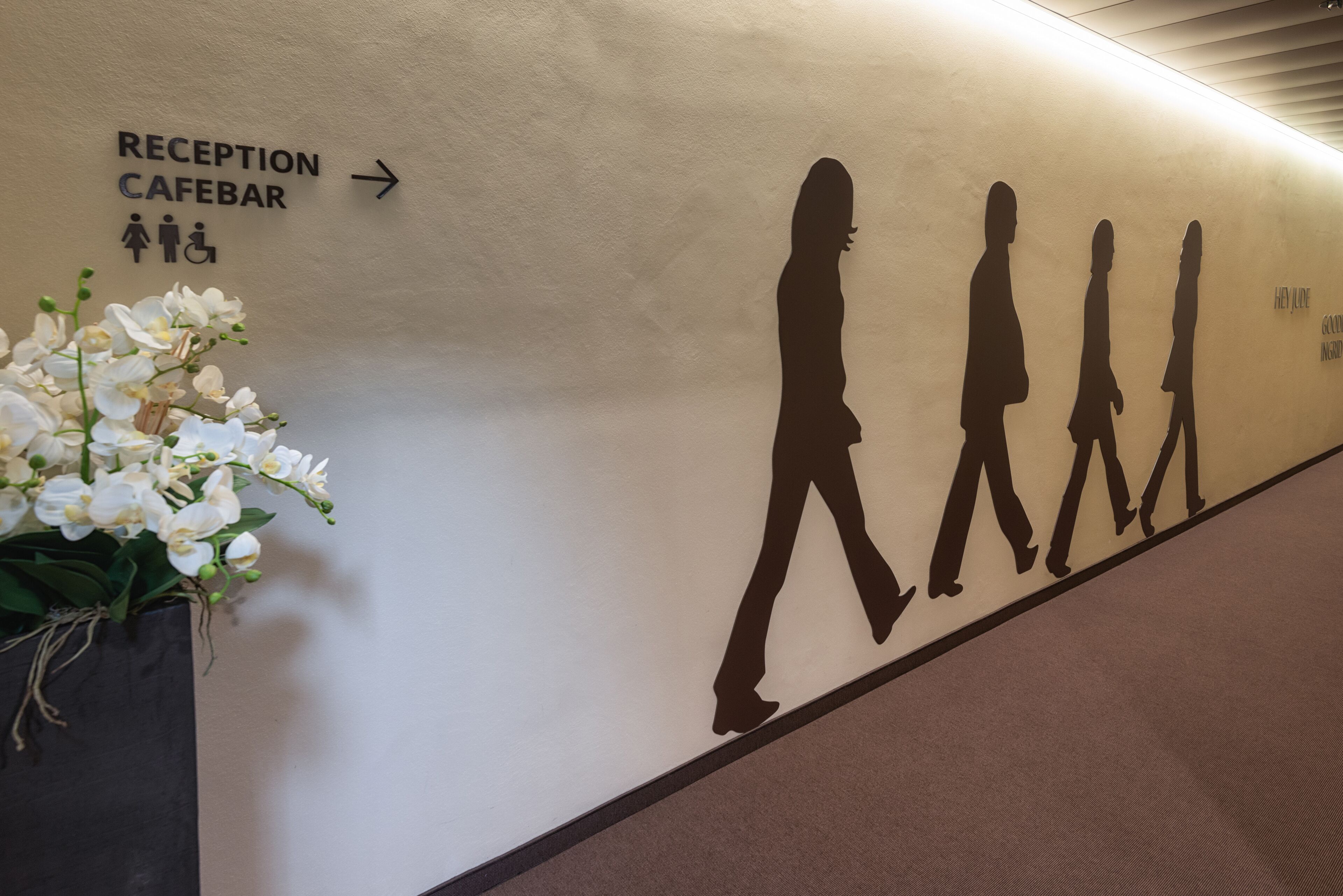 A reception area with a directional sign to the reception and cafe bar, and silhouettes of people walking.