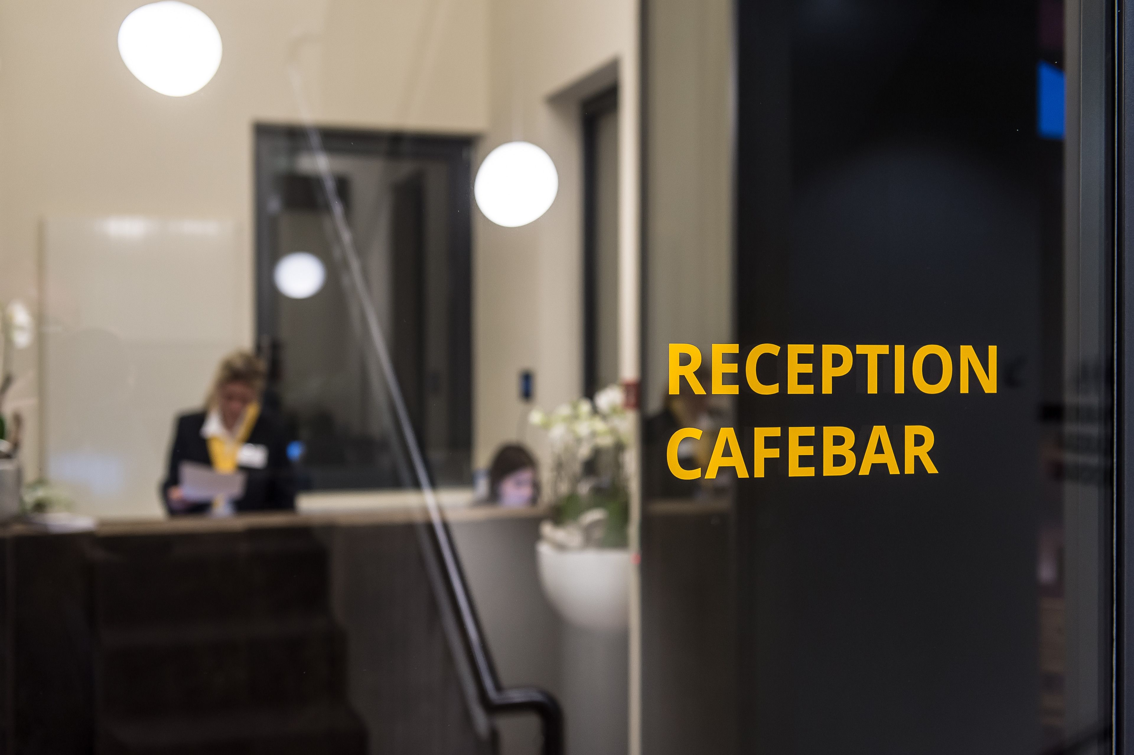 Un'area reception con una receptionist dietro il bancone, una pianta in vaso e una scala.