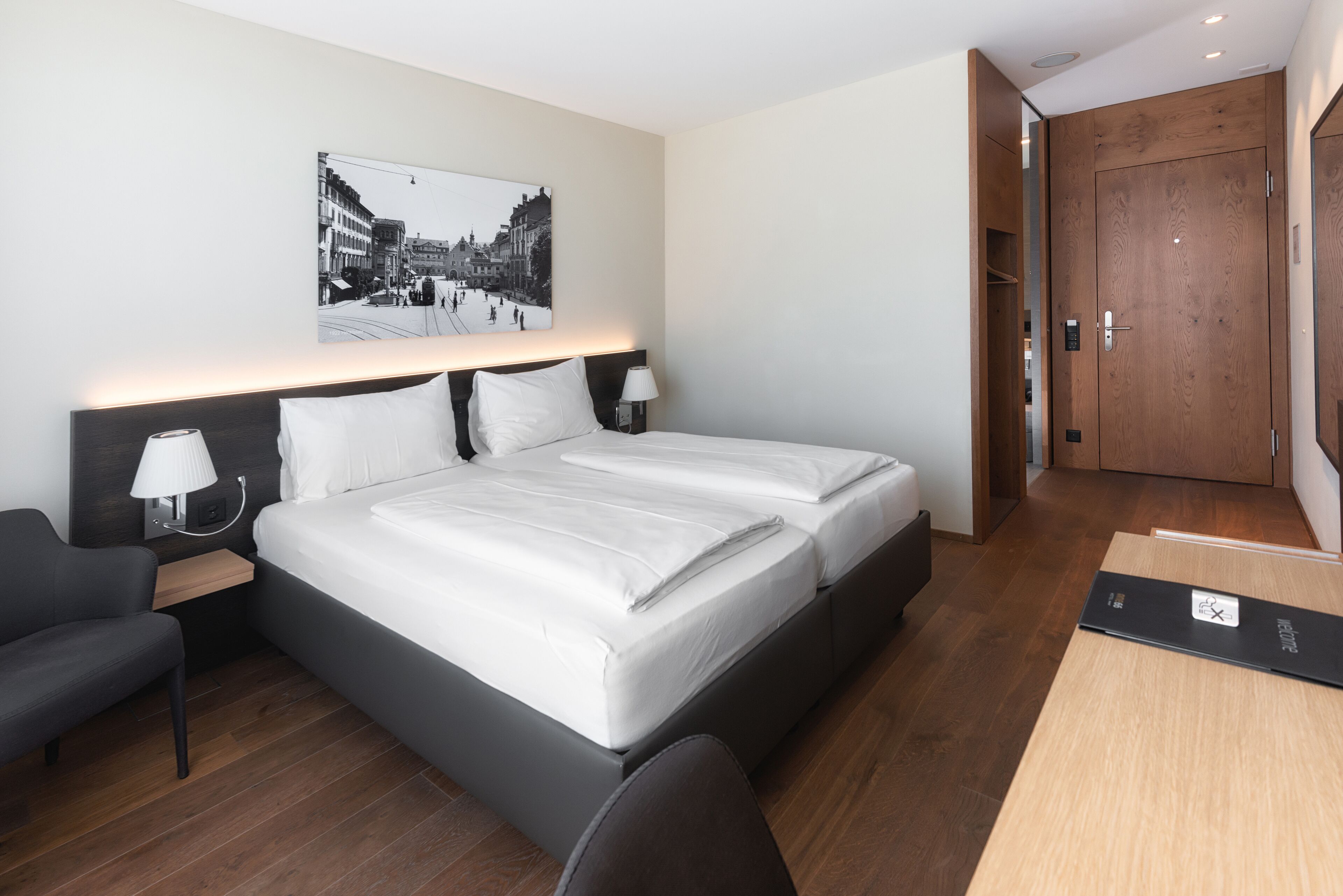 Habitación de hotel con una cama grande, mesitas de noche con lámparas, un escritorio y un armario de madera.