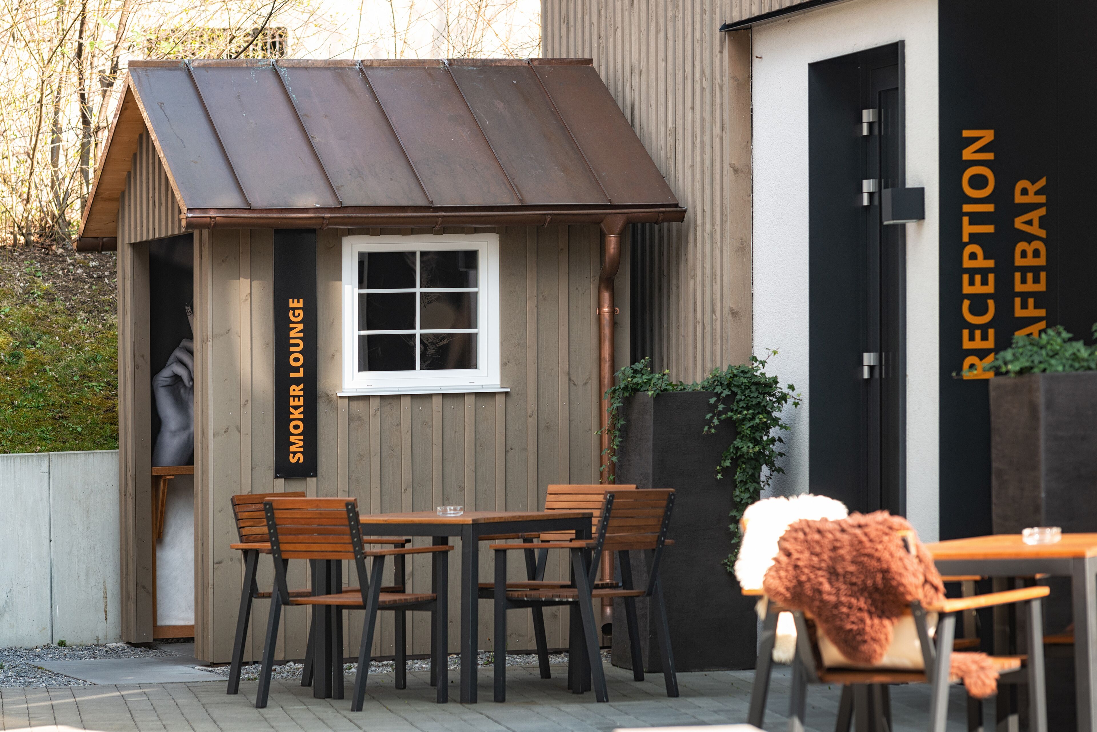 A reception bar with a wooden exterior and a small lounge area with tables and chairs.