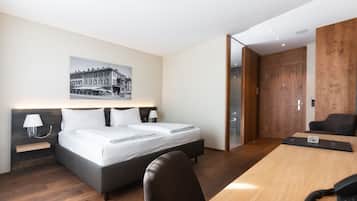 A modern hotel room with a large bed, bedside tables, a desk, and a wooden wardrobe.