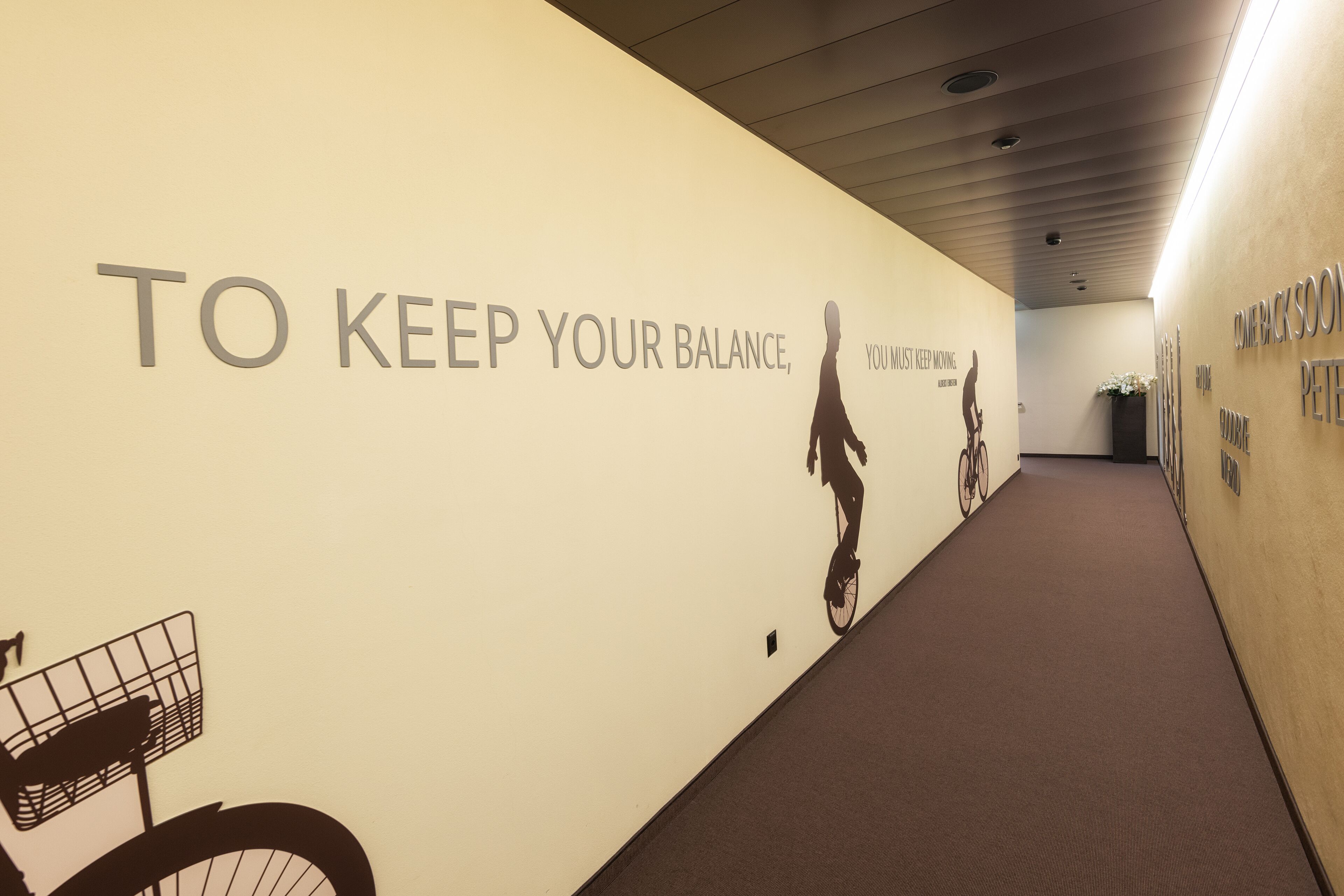 Un pasillo con una frase motivacional en la pared, una silueta de bicicleta y un cubo de basura.