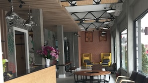 A modern interior with a wooden reception desk, a central seating area with a round table, and a brick wall with framed artwork. - Bed@Town Hostel (Bangkok)