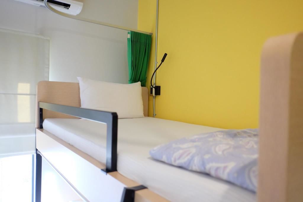 A single bed with a wooden frame, white bedding, and a green curtain on the window.