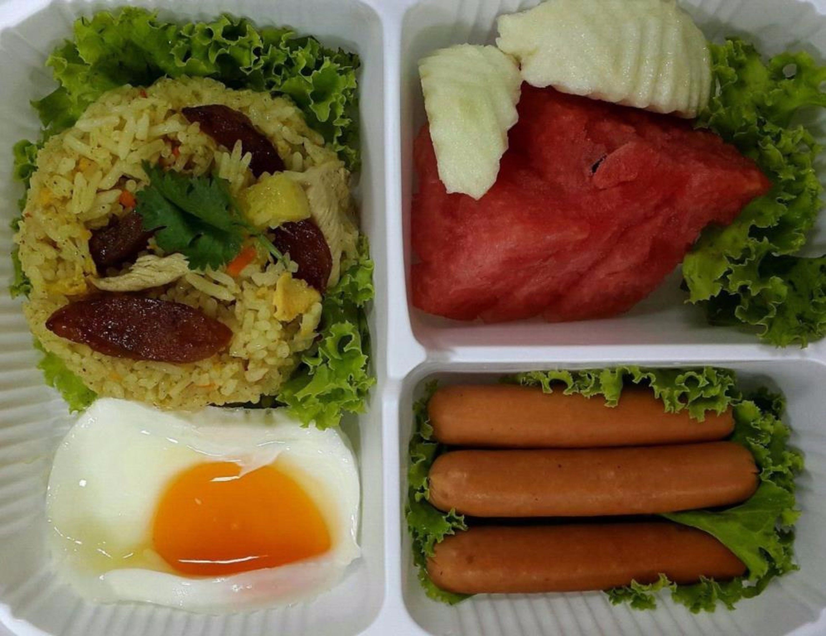 A meal with rice, egg, and sausages, and a side of watermelon and hot dogs.