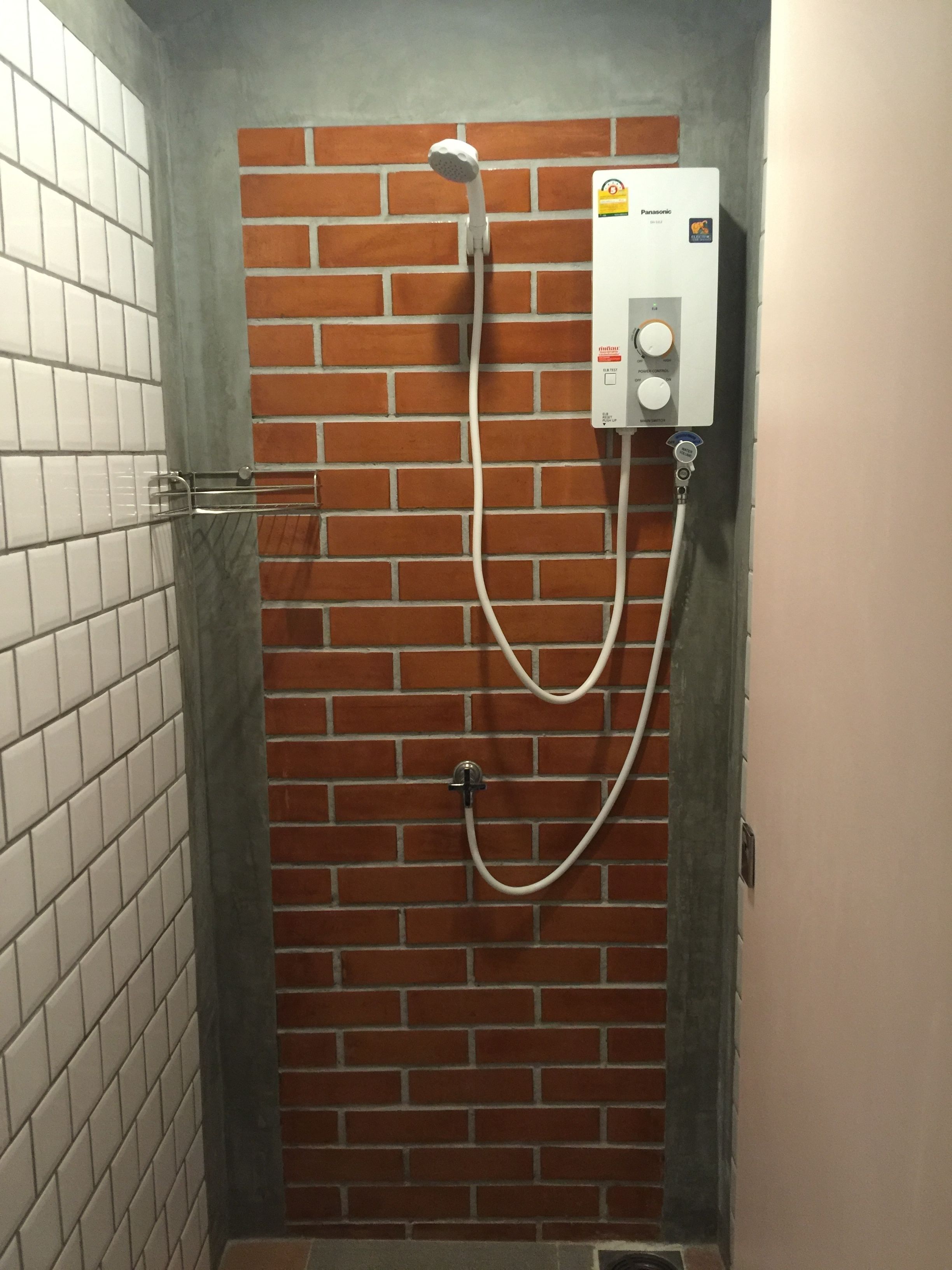 A shower area with a brick wall, a tiled floor, and a control panel.