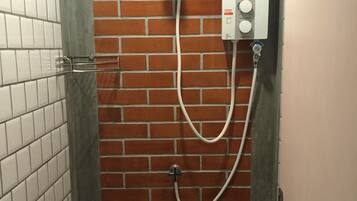 A shower area with a brick wall, a tiled floor, and a control panel.