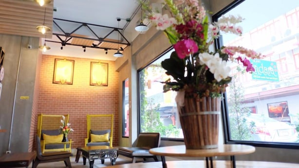 A cozy indoor seating area with brick walls, yellow cushioned chairs, and a large window offering a view of the street. - Bed@Town Hostel (Bangkok)