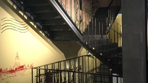 A staircase with a metal railing, a wall with a mural, and a ceiling with exposed beams. - Bed@Town Hostel (Bangkok)