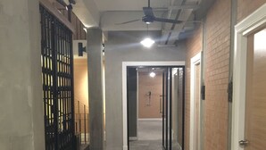 A hallway with a ceiling fan, a trash bin, and a door leading to another room. - Bed@Town Hostel (Bangkok)