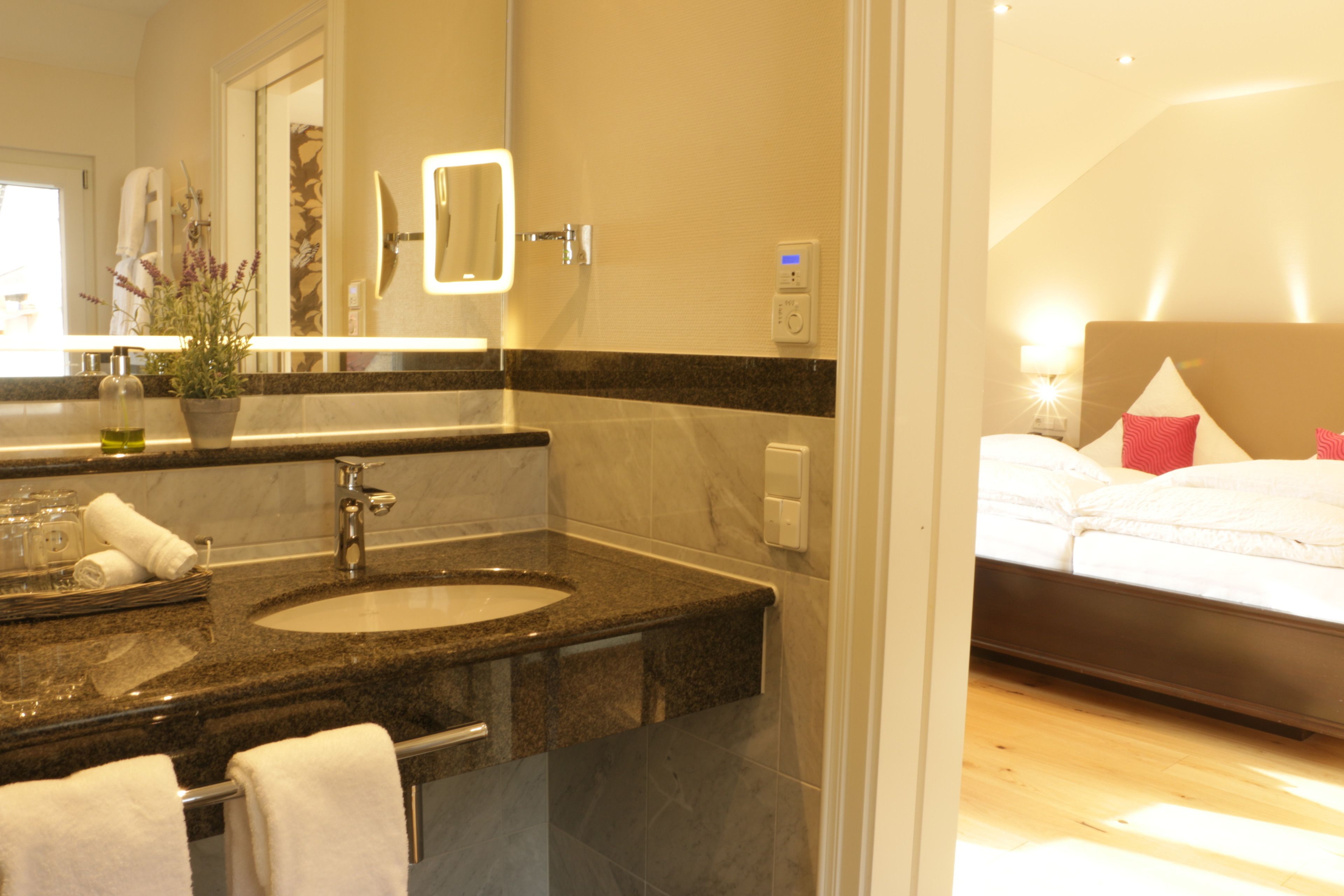 A modern bathroom with a granite countertop, a sink, and a mirror. There is a potted plant on the counter and a towel rack with towels.