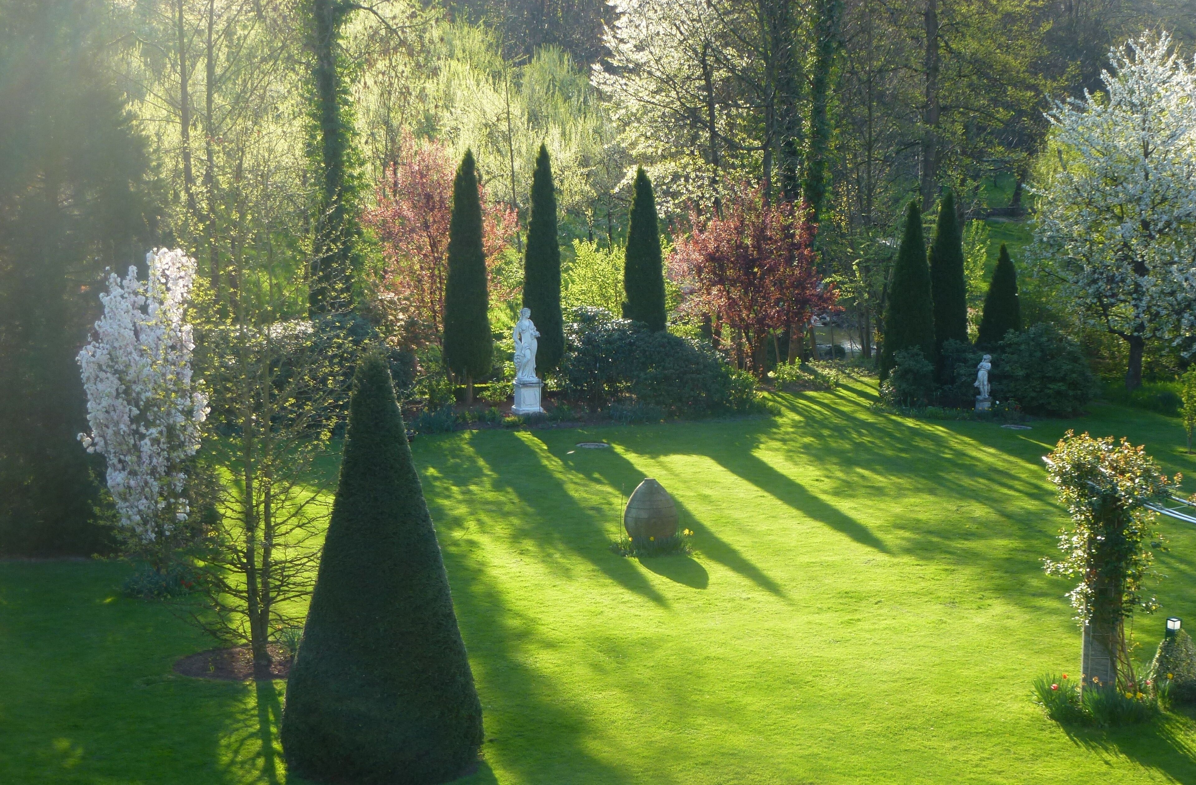 A well-manicured garden with statues, neatly trimmed hedges, and a variety of trees.