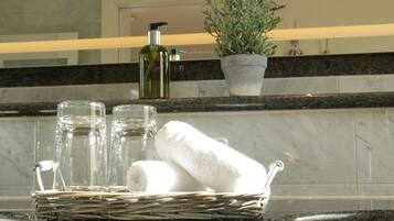 Une salle de bain avec un comptoir en marbre, un flacon de lotion, une plante en pot et un panier contenant des serviettes et des verres.