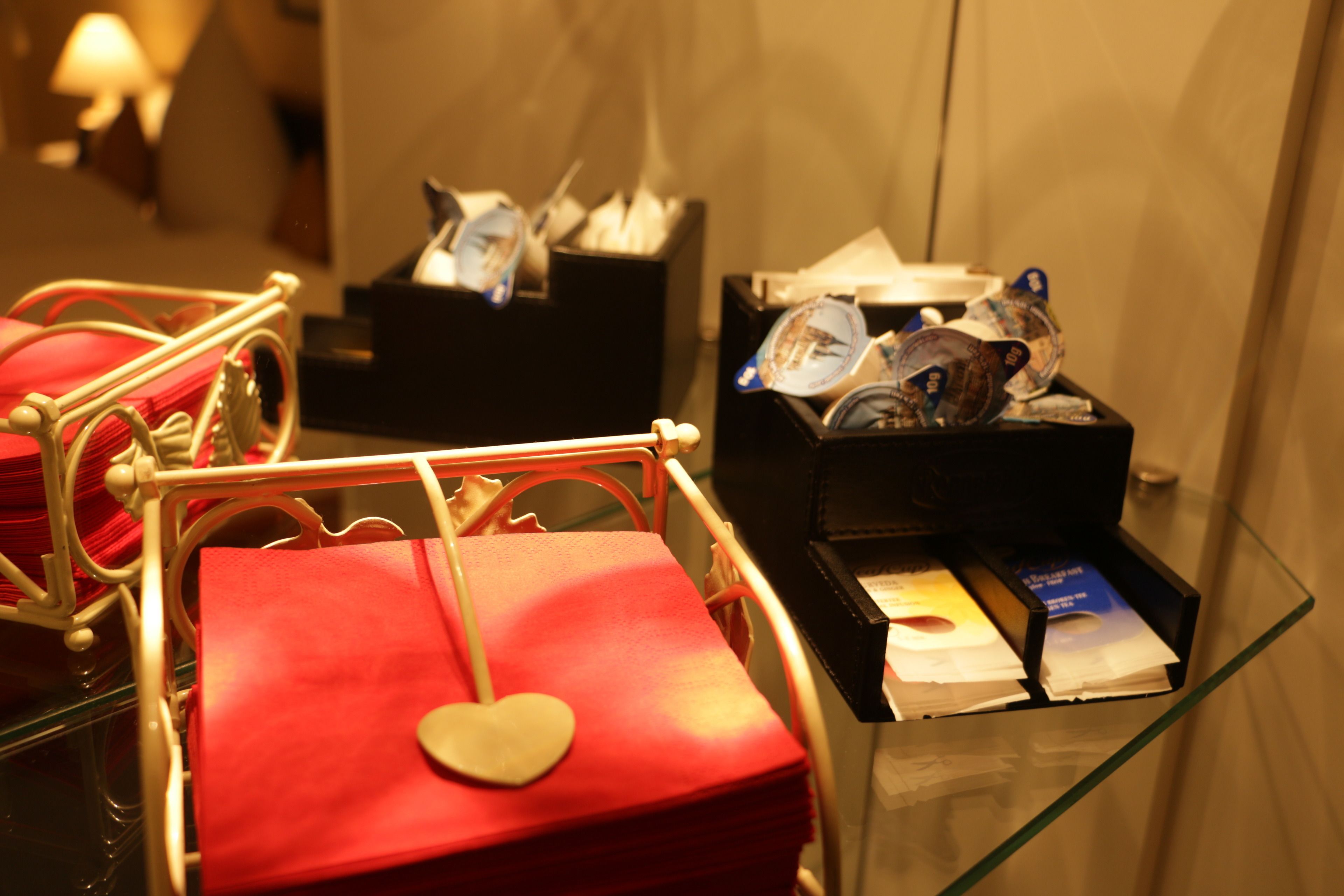 Ein Hotel-Empfangsbereich mit einer Glastheke, die verschiedene Gegenstände zeigt, darunter eine rote Geschenkbox mit herzförmiger Verzierung und eine schwarze Box mit Broschüren.
