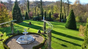 A well-manicured garden with a central fountain, neatly trimmed hedges, and a variety of trees. - Baumanns Landhaus Durbach (Durbach)