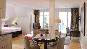 A modern bedroom with a bed, a dining table with chairs, and a large window with curtains. - Baumanns Landhaus Durbach (Durbach)