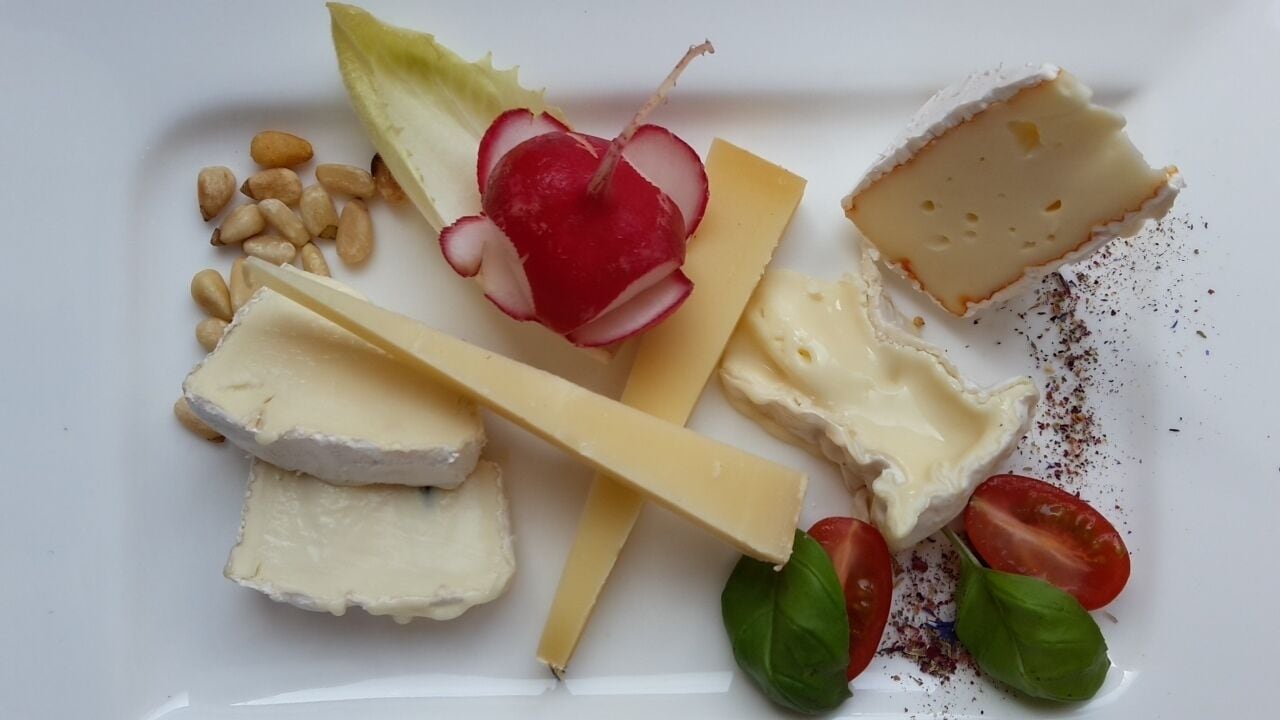 A plate with various cheeses, radishes, pine nuts, and cherry tomatoes.