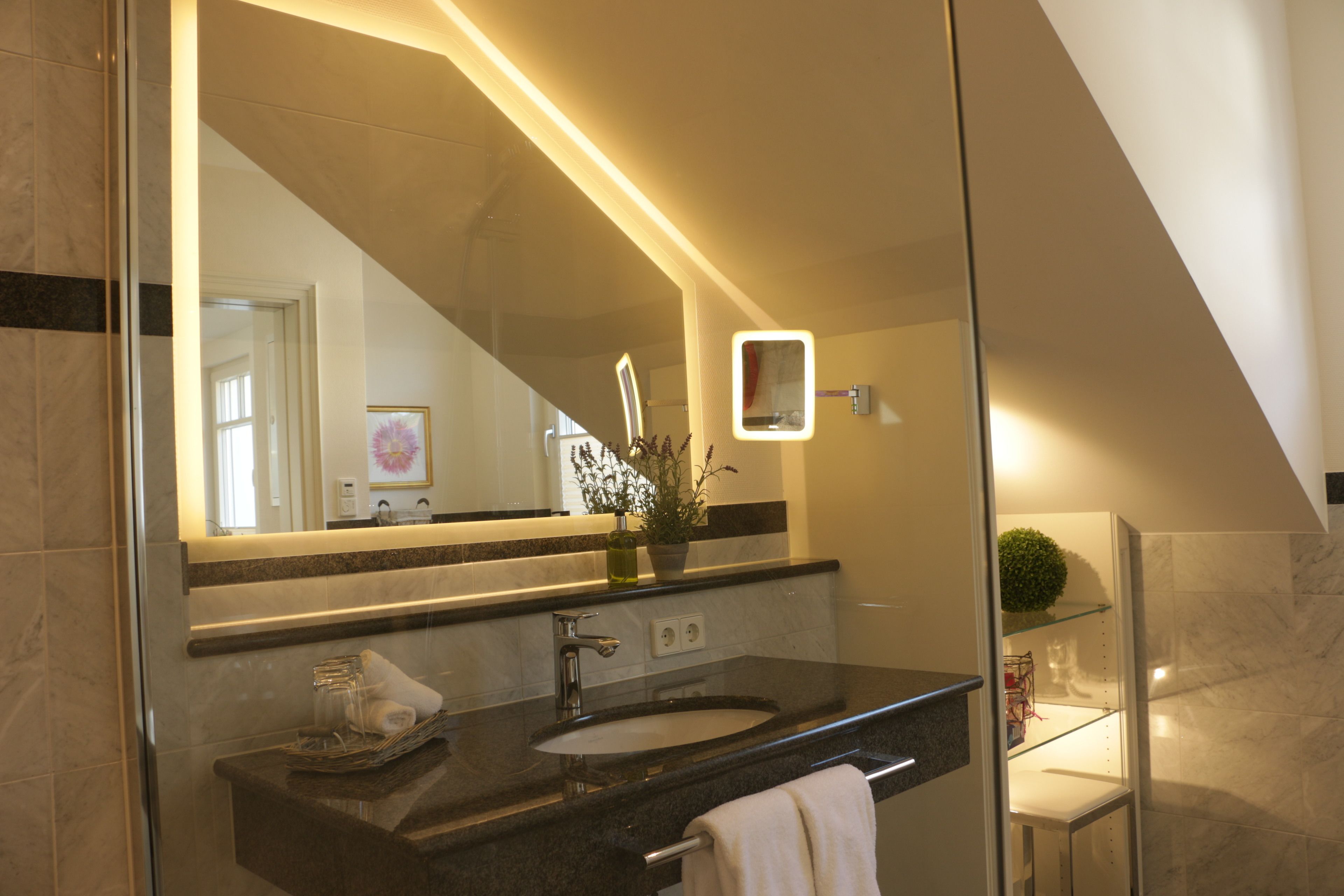 A modern bathroom with a glass-enclosed shower, a marble sink, and a large mirror with integrated lighting.