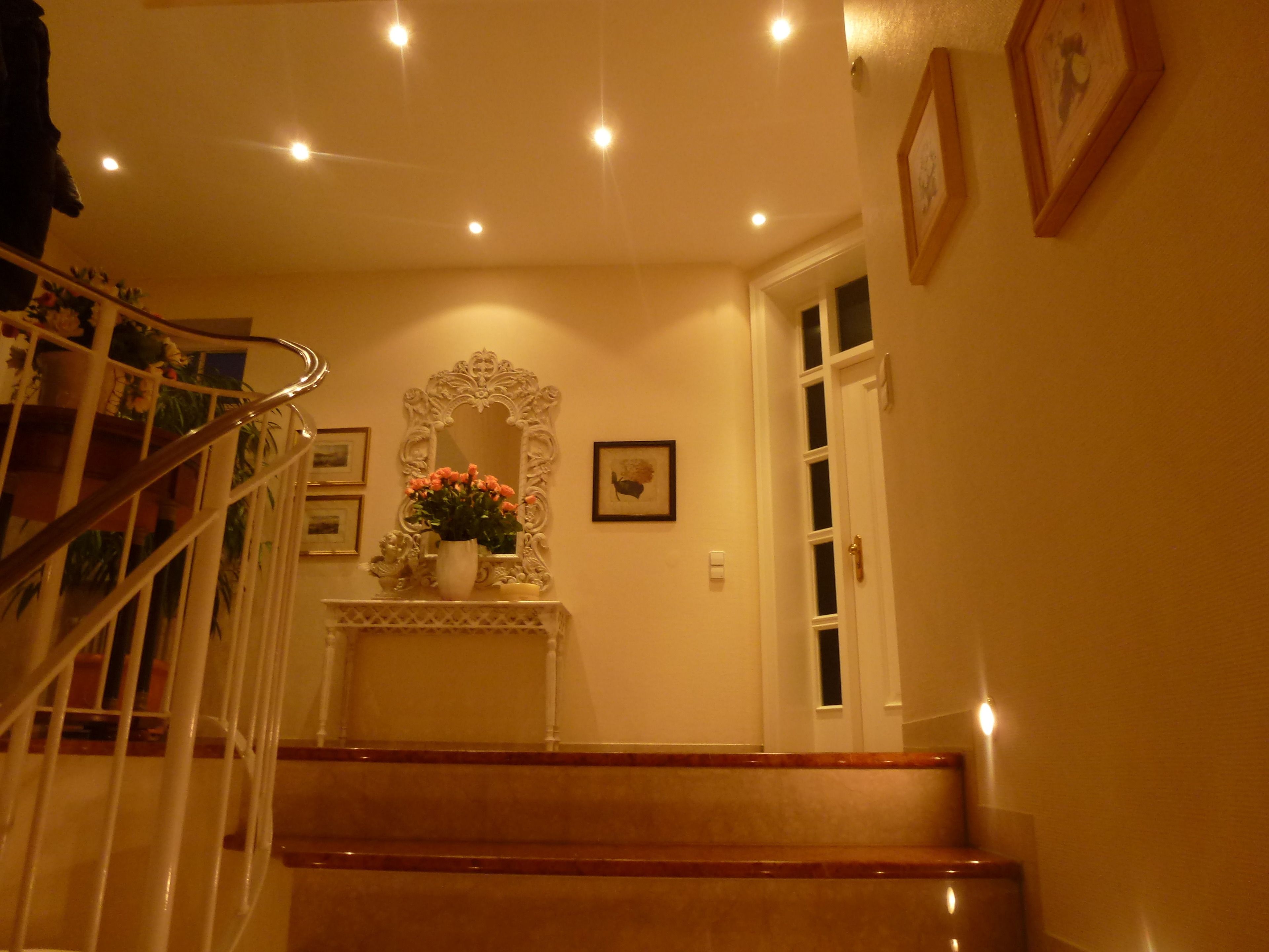 Eine Treppe mit weißer Brüstung führt zu einer Empore mit einer weißen Blumenvase und einem Spiegel.