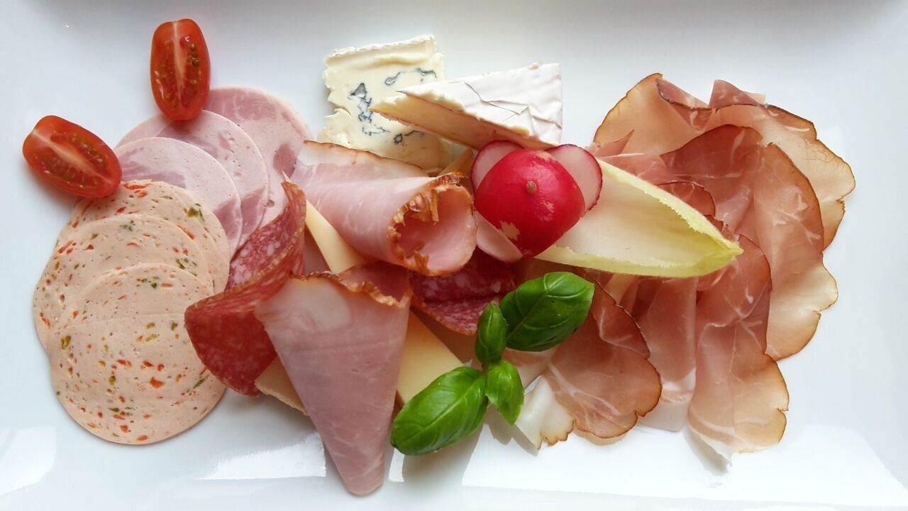 A charcuterie board with various meats, cheese, and vegetables.