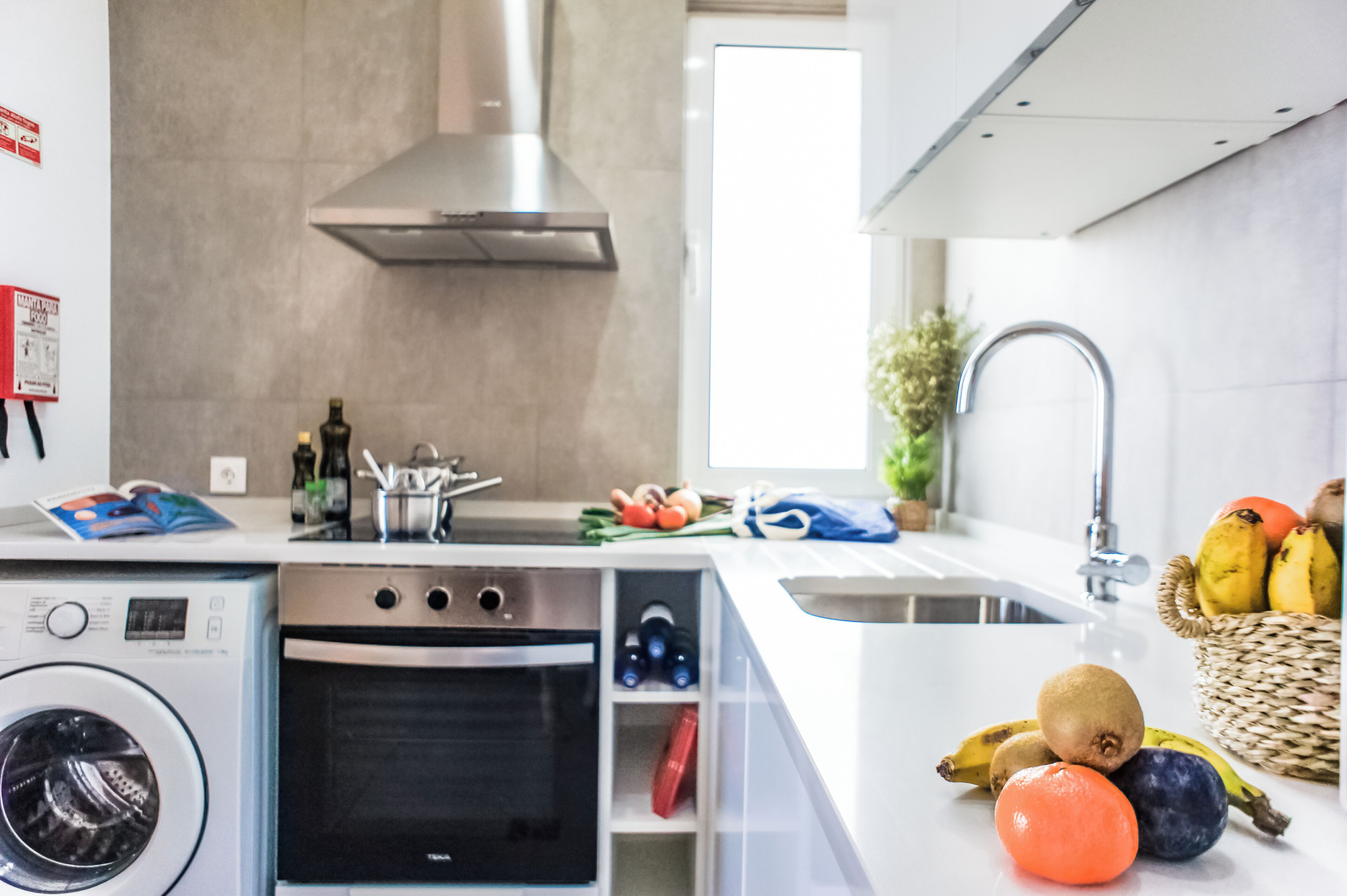 Une cuisine moderne dotée d’un four encastré, d’une hotte en acier inoxydable, d’un évier et d’un panier à fruits.