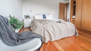 Un dormitorio con cama, una silla, una planta pequeña y un armario de madera.