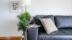 Una sala de estar moderna con un sofá de cuero oscuro, una lámpara de pie, una pequeña planta en maceta y cuadros en la pared.