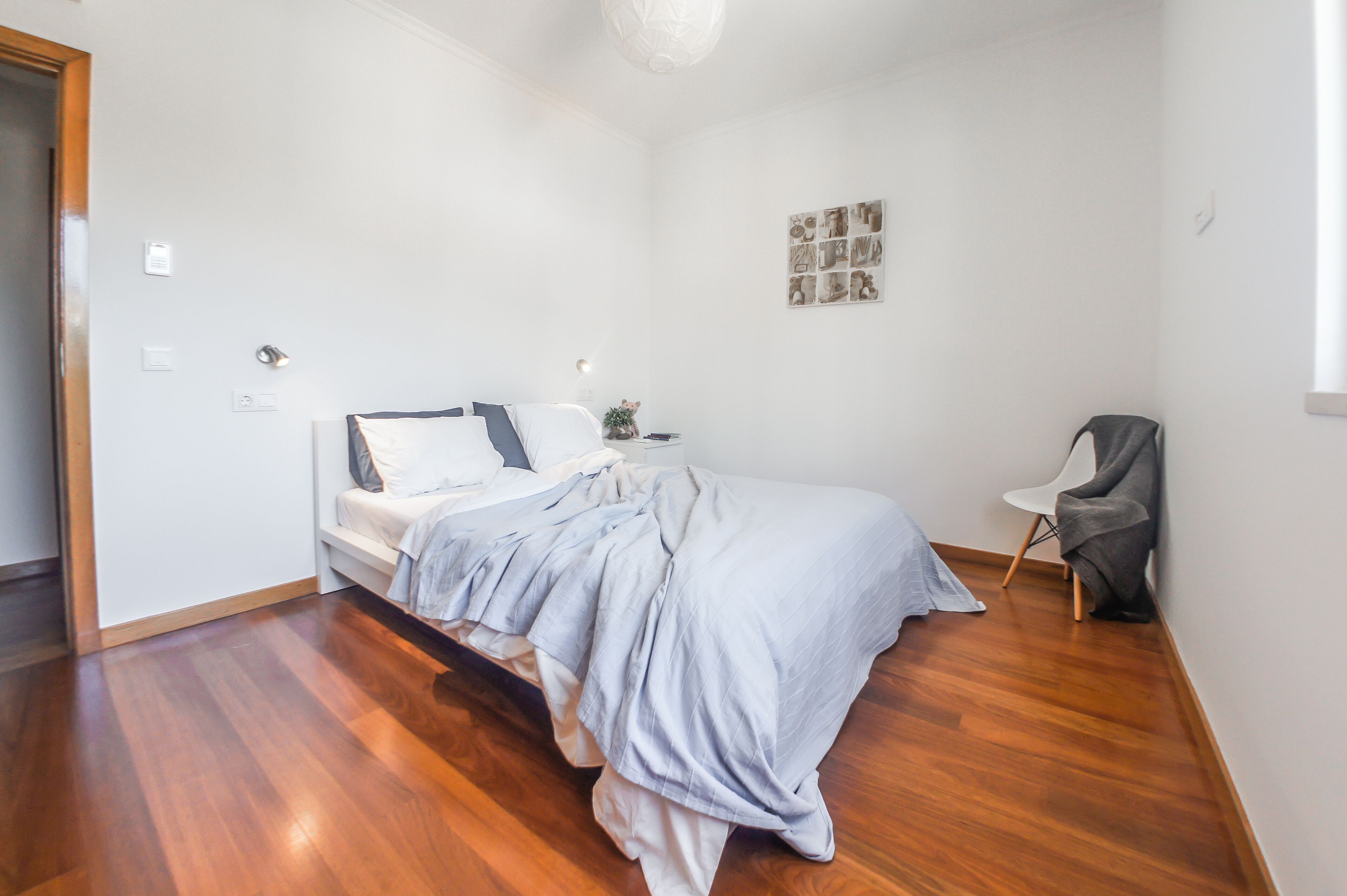 A bedroom with a bed, a chair, a nightstand, and a wall art piece.