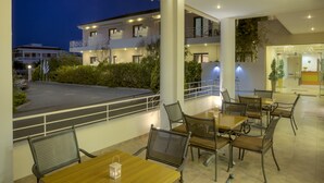 A modern outdoor seating area with tables and chairs, a view of a building across the street, and a well-lit environment. - Kyniska Hotel (Monemvasia)