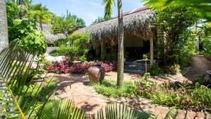 A tropical garden with a thatched-roof structure, lush greenery, and a stone pathway. - Red Flower Cottages Homestay (Da Nang)