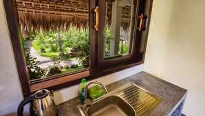 A kitchen with a window view of a garden, a stainless steel sink, and a kettle. - Red Flower Cottages Homestay (Da Nang)