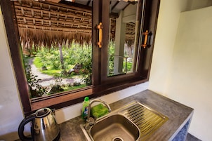 Una cocina con vista al jardín por una ventana, un lavamanos de acero inoxidable y una tetera.
